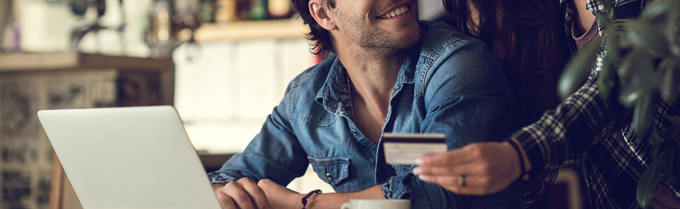 Man at laptop smiling next to woman holding debit card
